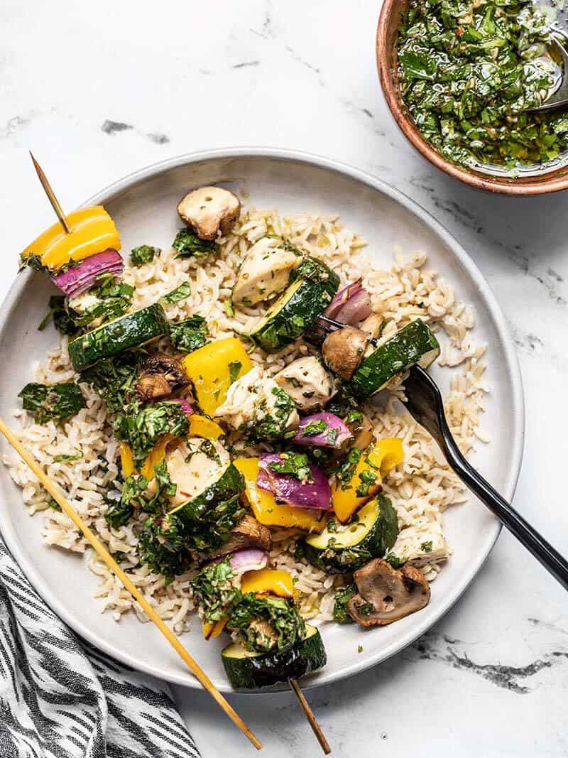 Chicken and vegetables removed from one chimichurri chicken kebab, on a bed of rice with a fork.