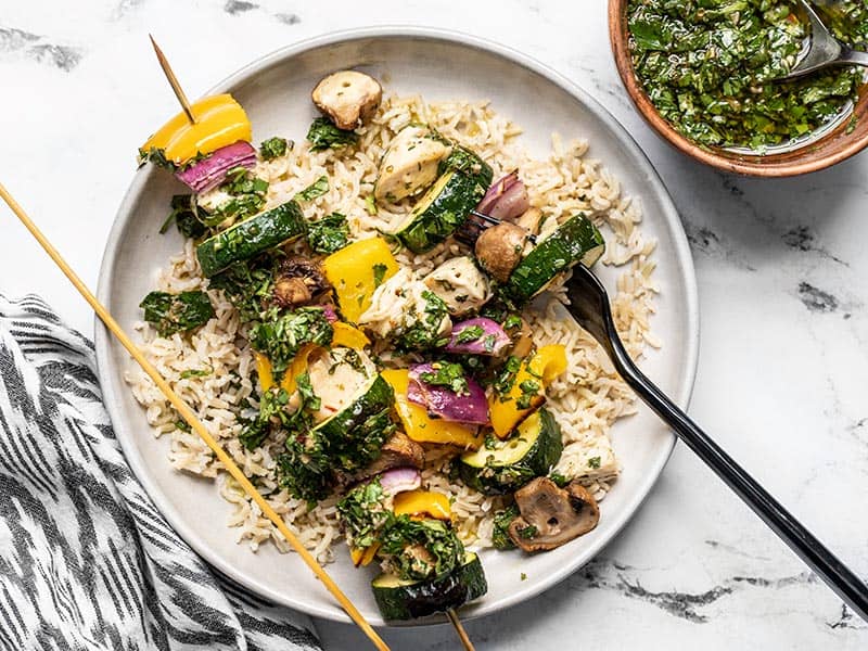 Chicken and vegetables removed from one skewer of a chimichurri chicken kebab, on a bed of rice.