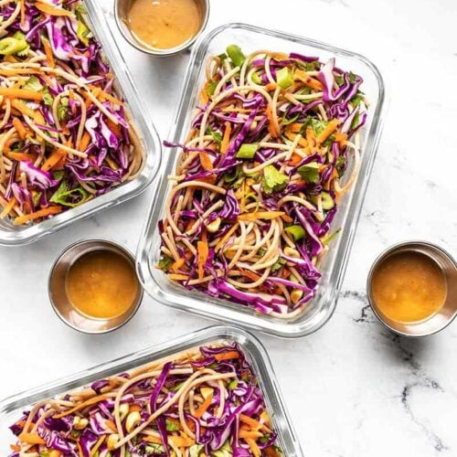 Three glass meal prep containers full of cold peanut noodle salad, dressing containers on the side.