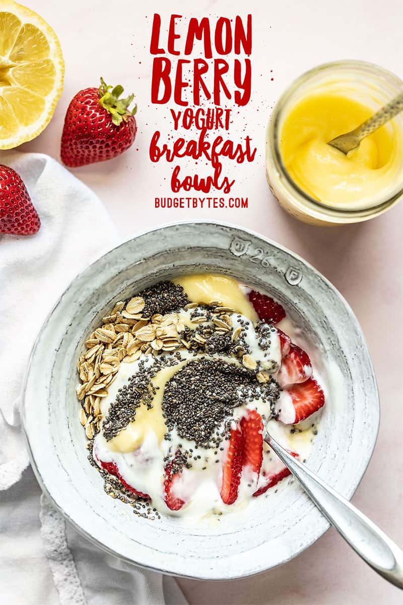 A half stirred Lemon Berry Yogurt Breakfast Bowl with strawberries and lemon curd on the side.