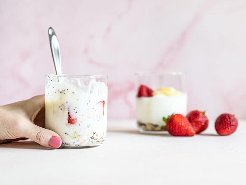 Two cups full of lemon berry yogurt breakfast bowls, one with a spoon and being held at the base by a hand.