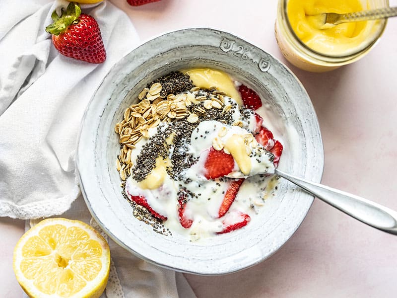 A half stirred Lemon Berry Yogurt Breakfast Bowl with a cut lemon and some strawberries near by.