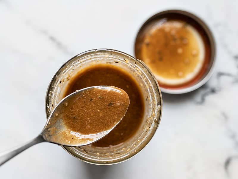 Parmesan Balsamic Vinaigrette on a spoon over the jar full of dressing