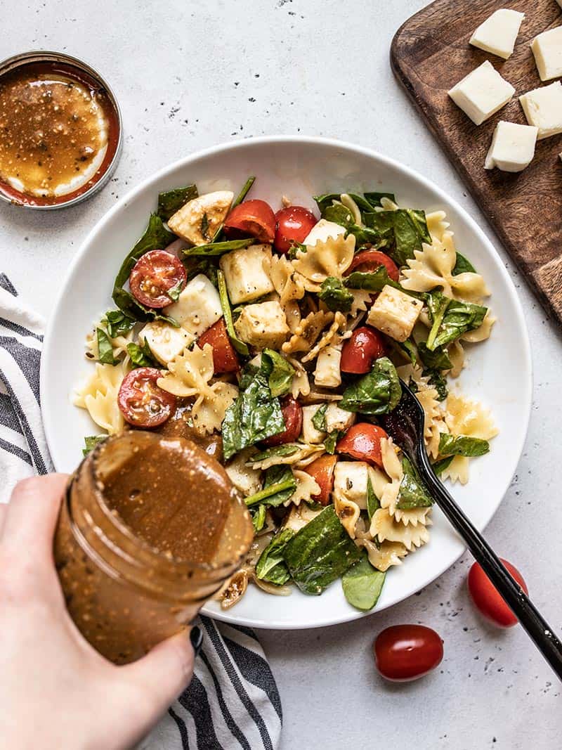 Dressing being poured onto a bowl of tomato mozzarella pasta salad.