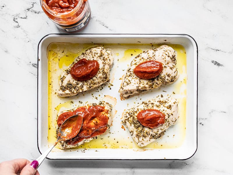 Pizza sauce being spread over the baked chicken pieces.