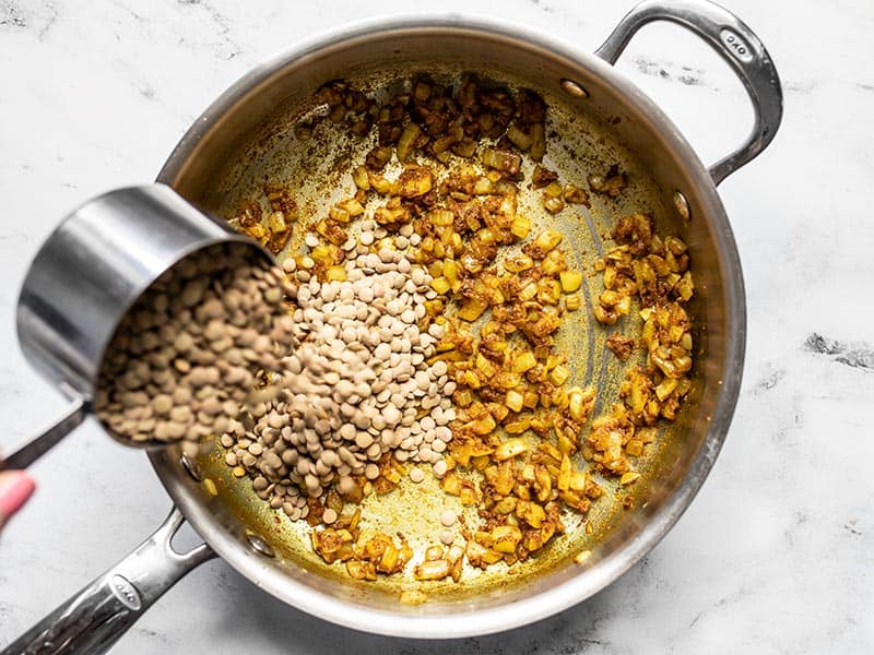 Dry lentils being poured into the skillet