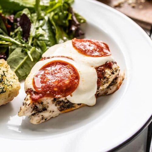 Front view of a piece of Baked Pizza Chicken on a plate with salad and garlic bread.