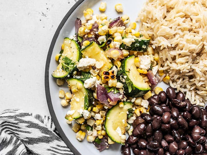 Close up of Charred Corn and Zucchini Salad on a plate with black beans and rice.