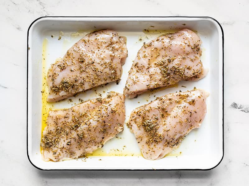 Chicken coated in herbs and oil in a baking dish.