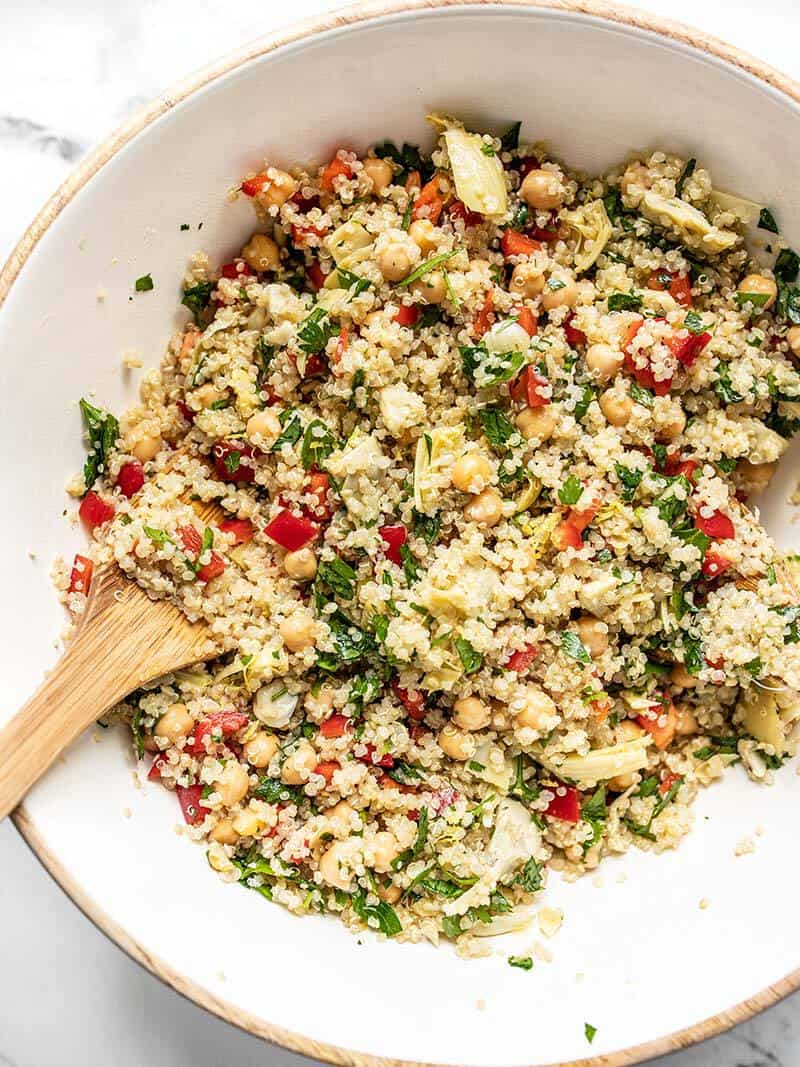 Close up of finished Lemony Artichoke and Quinoa Salad in the mixing bowl with wooden salad tongs