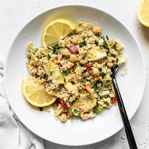 Overhead view of Lemony Artichoke and Quinoa Salad in a bowl with lemon wedges and a fork.