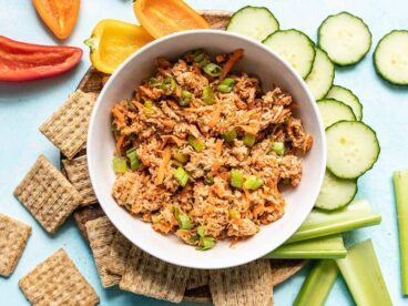 A bowl of Sweet and Spicy Tuna Salad surrounded by crackers and vegetables.