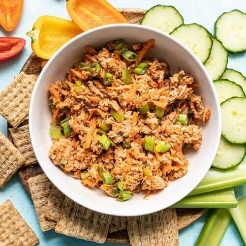 A bowl of Sweet and Spicy Tuna Salad surrounded by crackers and vegetables.