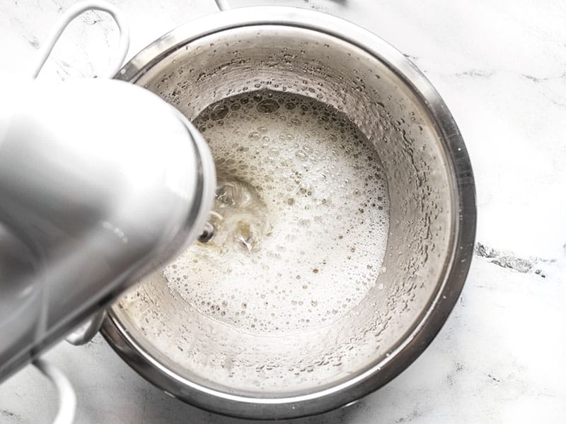 Aquafaba slightly whipped in a metal bowl with a hand mixer.