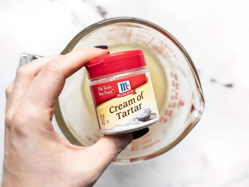 Cream of tartar container held over the measuring cup with aquafaba