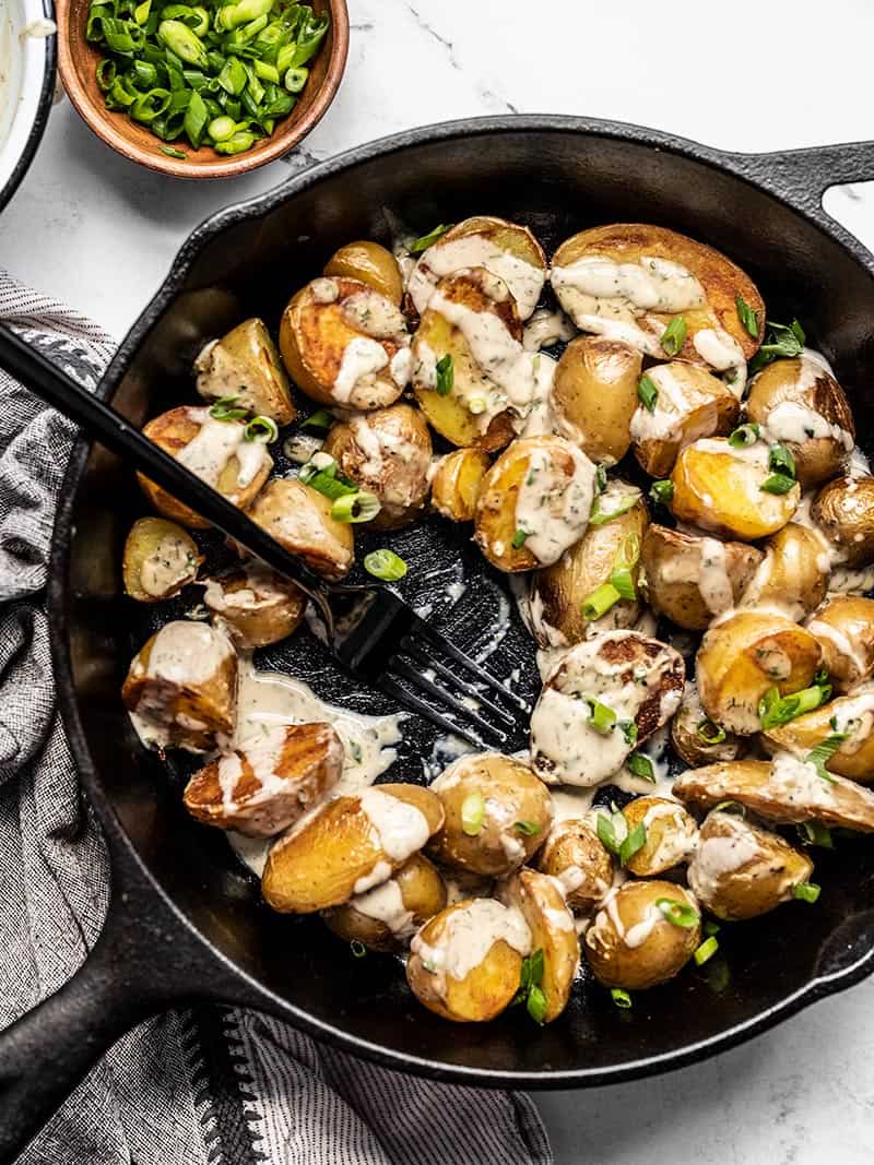 Half eaten skillet of crispy potatoes with lemon dill tahini dressing and green onions