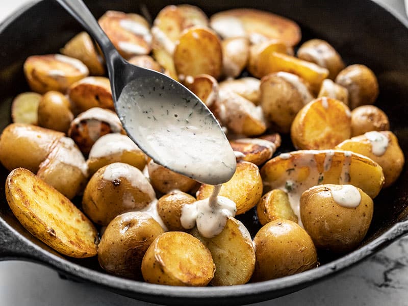 tahini dressing being drizzled over potatoes, close up 