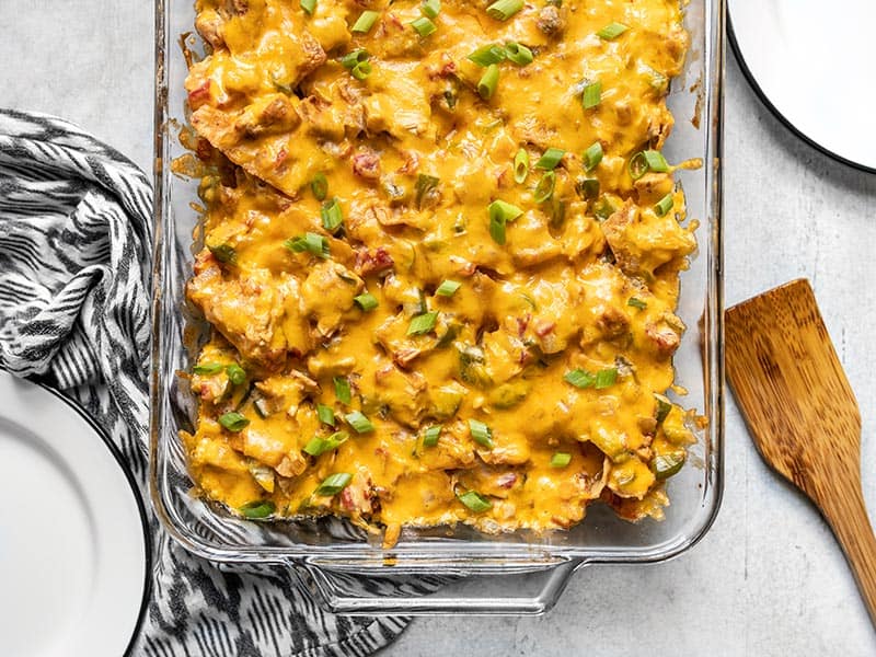 Overhead view of the bottom half of the casserole dish with baked King Ranch Chicken Casserole and two empty plates on the sides