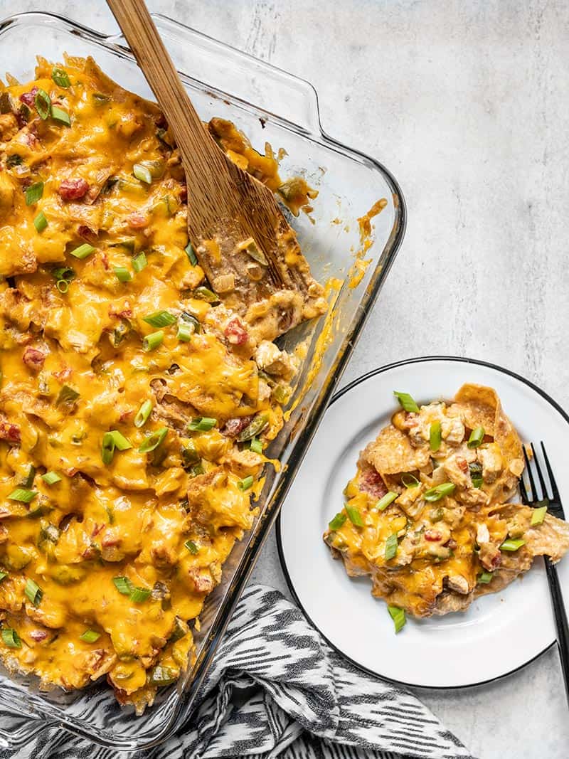 A casserole dish with baked King Ranch Chicken Casserole next to a plate with a serving dished out.