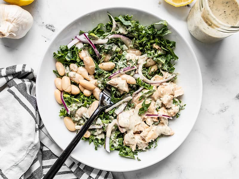 Half stirred Lemon Dill Salmon and Kale Salad with a black fork and jar of dressing on the side.