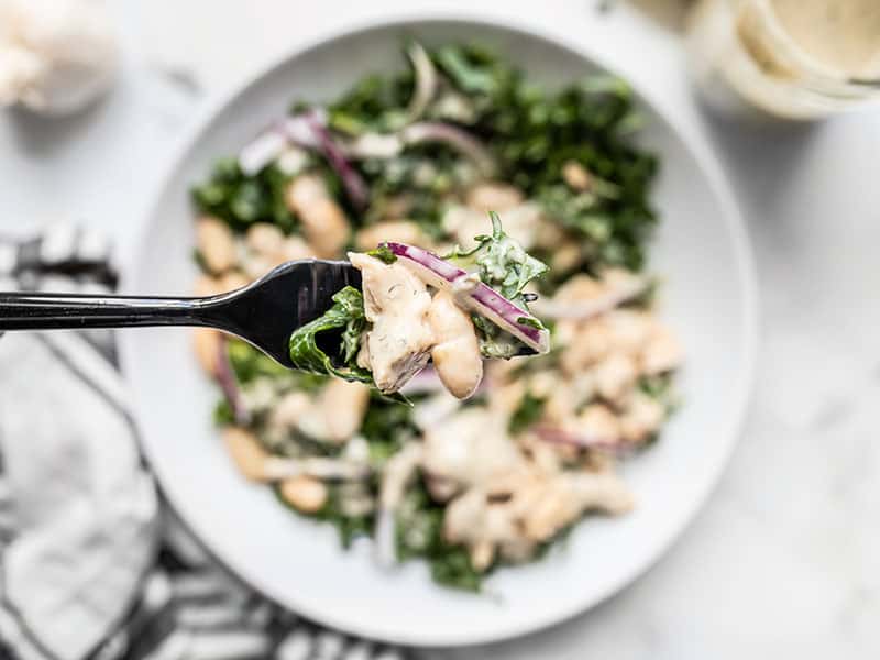 Close up of a forkful of Lemon Dill Salmon and Kale Salad with the salad bowl in the background