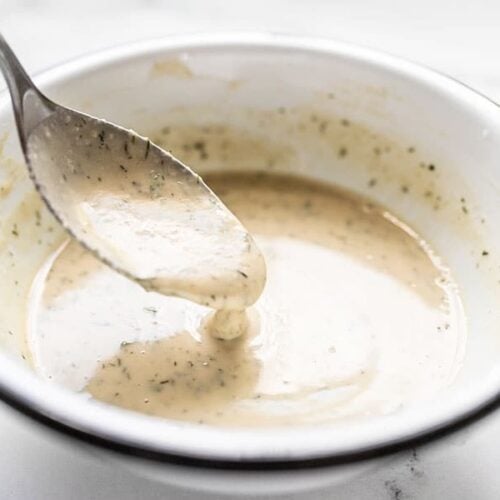 Lemon Dill Tahini Dressing dripping off a spoon into a white bowl.