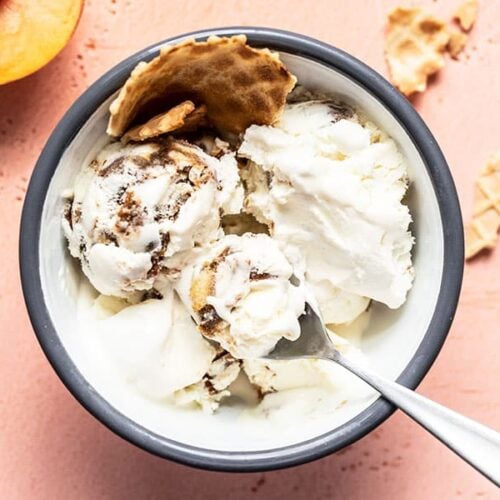 Overhead view of one bowl of no churn balsamic peach ice cream with waffle cone and a fresh peach on the side.