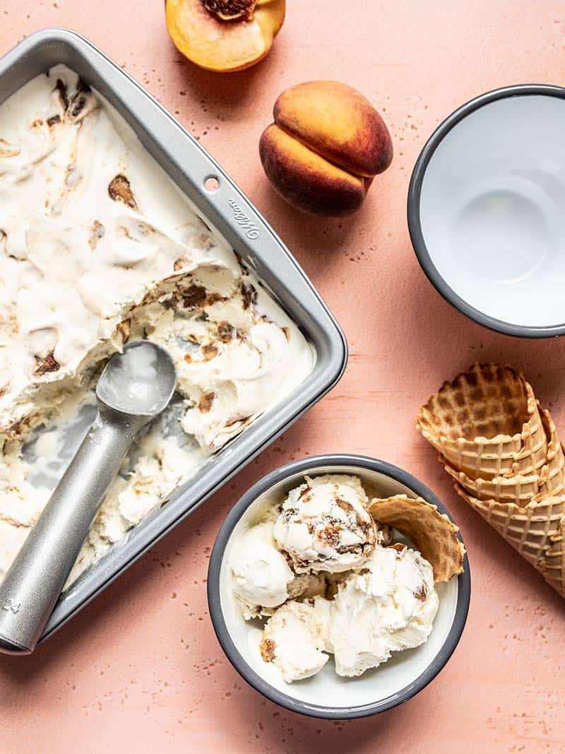 No Churn Balsamic Peach Ice Cream scooped out of the freezer dish into one out of two bowls, waffle cones on the side.