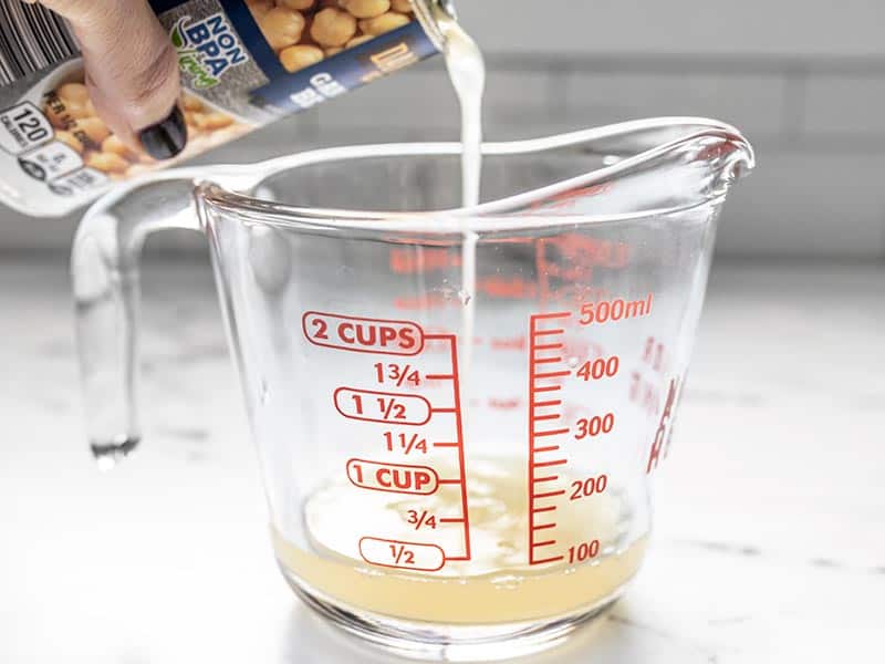 Pour aquafaba from the can of chickpeas into a measuring cup