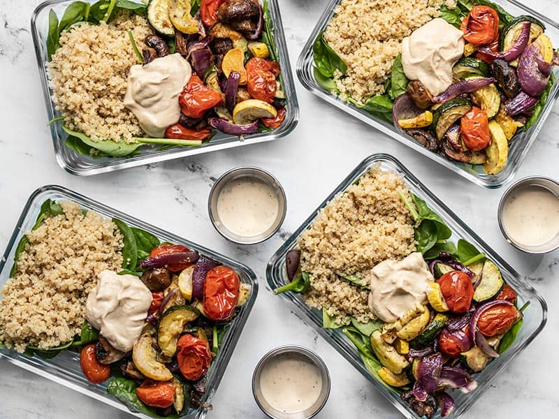 Four glass containers with Roasted Vegetable Salad and three dressing containers