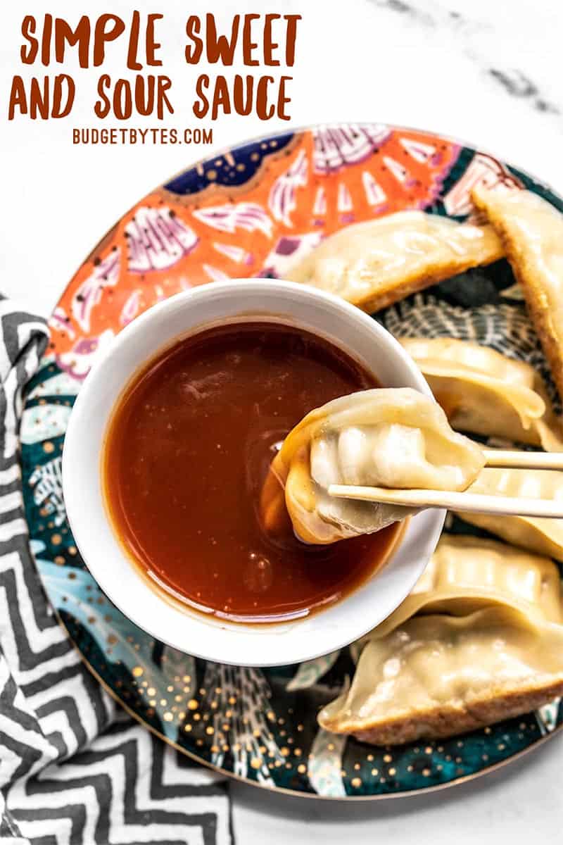 A dumpling being dipped into a bowl of sweet and sour sauce using chopsticks.