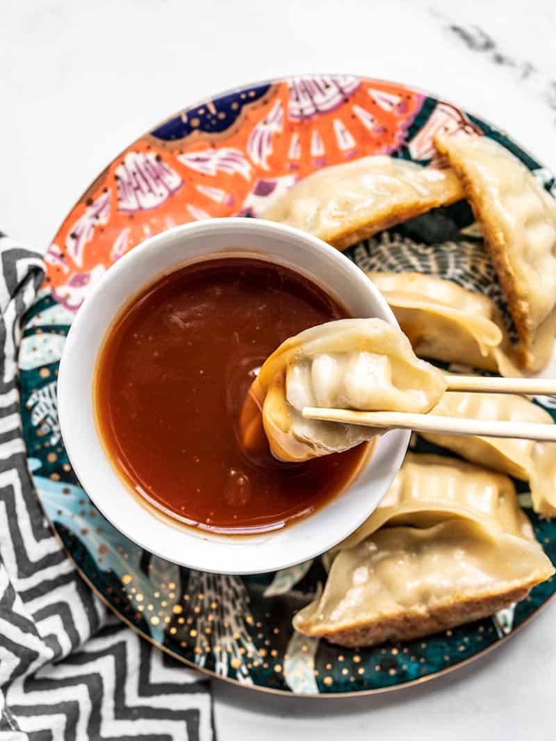 A dumpling being dipped into a bowl of Simple Sweet and Sour Sauce on a colorful plate.