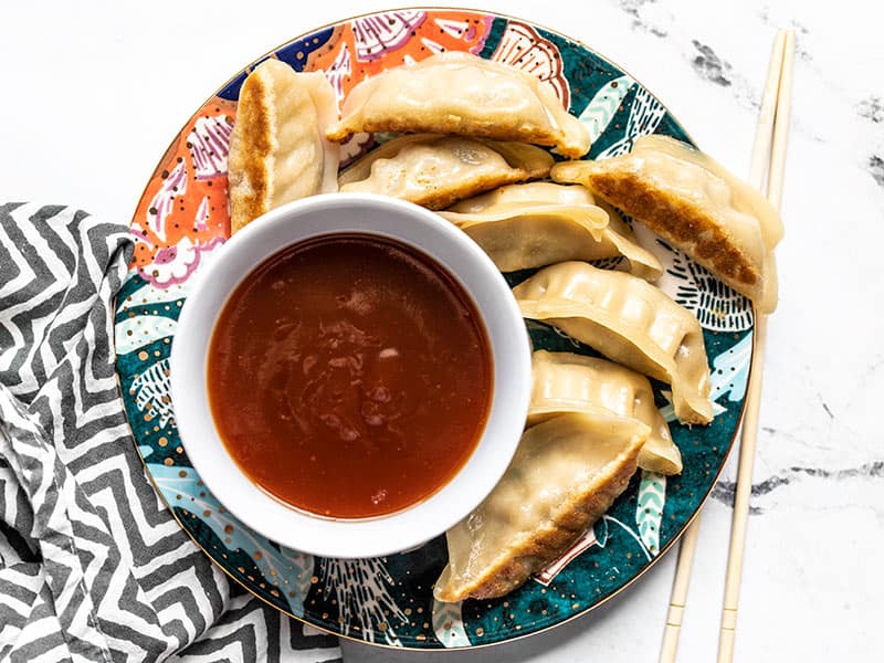 A bowl of Simple Sweet and Sour Sauce on a colorful plate with dumplings, chopsticks on the side.