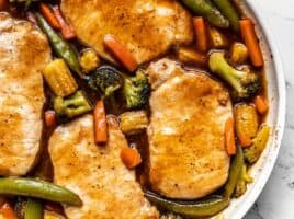 Close up overhead view of pork chops in the skillet with vegetables, covered with sweet and sour sauce.