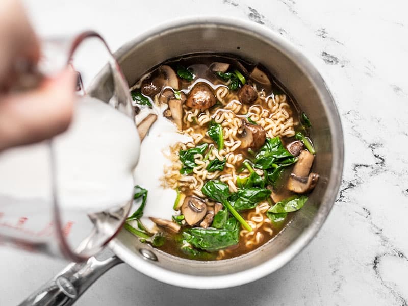 Coconut milk being poured into the ramen noodles in the pot