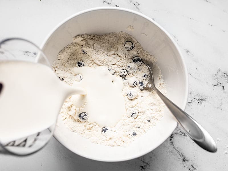 Heavy whipping cream being poured into the bowl of dry ingredients