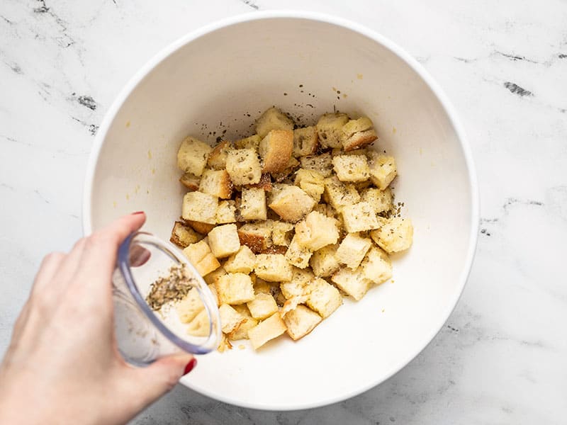 Herbs being sprinkled over bread cubes.