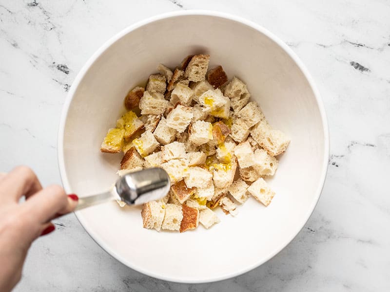 Oil being drizzled over bread cubes in a bowl