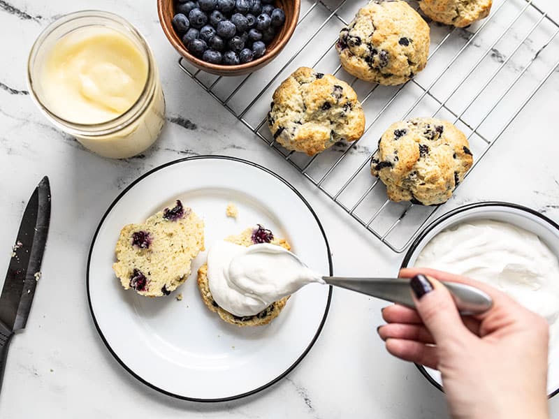 Blueberry lemon curd shortcakes being assembled, whipped cream being added to biscuit.