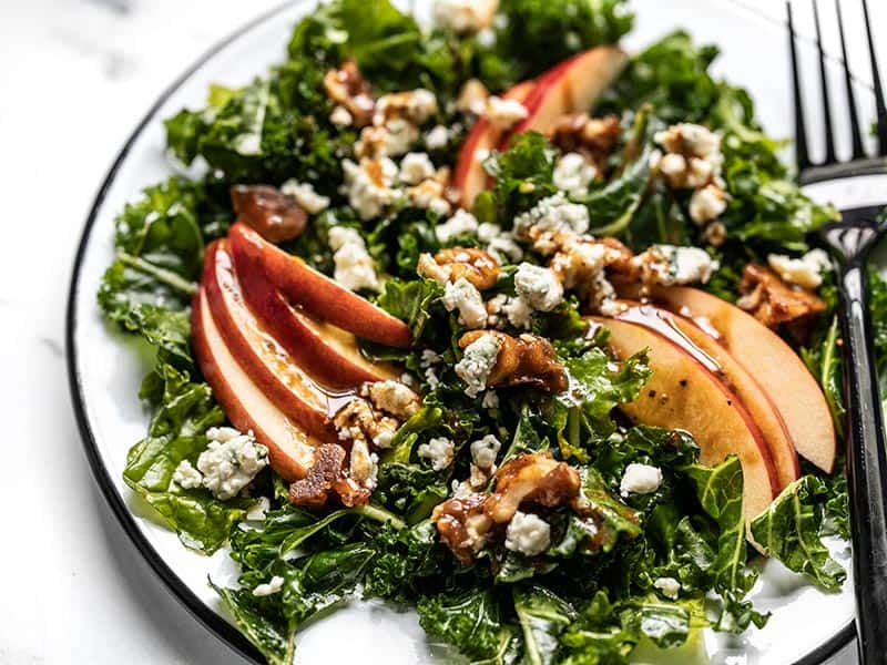 Close up side view of Autumn Kale and Apple Salad on the plate with dressing.