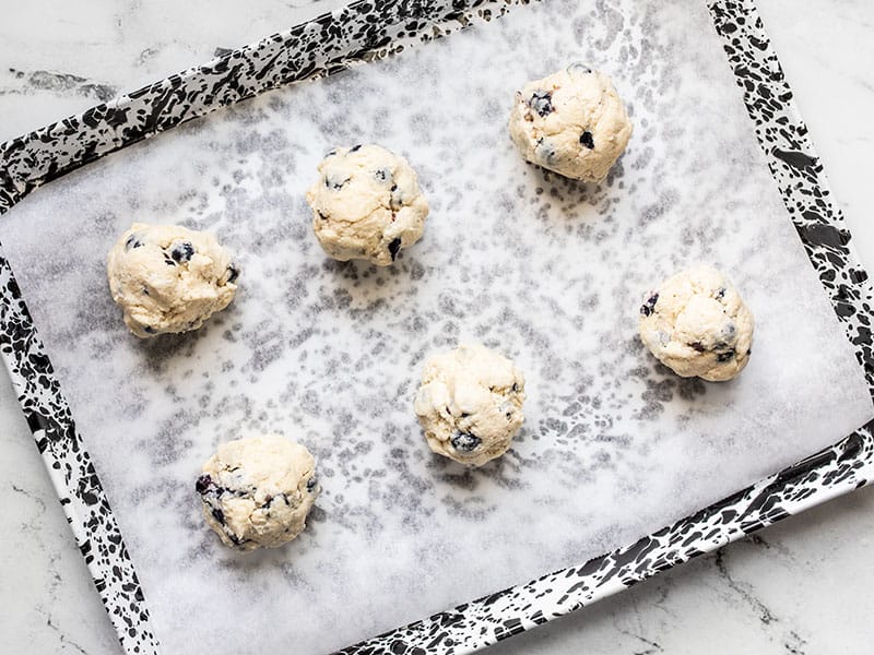 Blueberry biscuits ready to be baked on a parchment lined baking sheet.