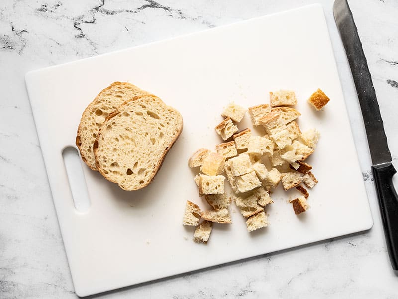 Cubed bread on a cutting board next to two slices of bread