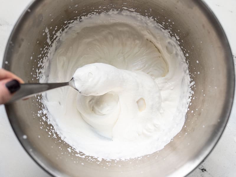 Homemade whipped cream being lifted on a spoon out of the metal bowl.