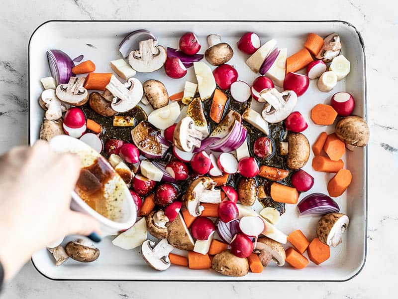 Balsamic marinade being poured onto prepared vegetables on the baking sheet