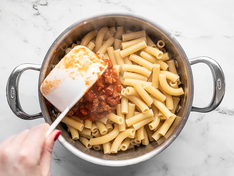 Sauce being added to cooked ziti in the pot.