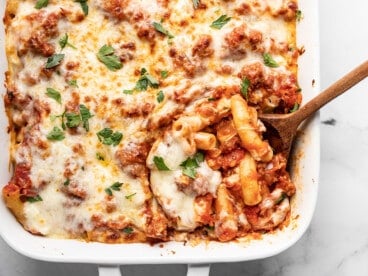 Overhead view of baked ziti being scooped out of the casserole dish with a wooden spoon.