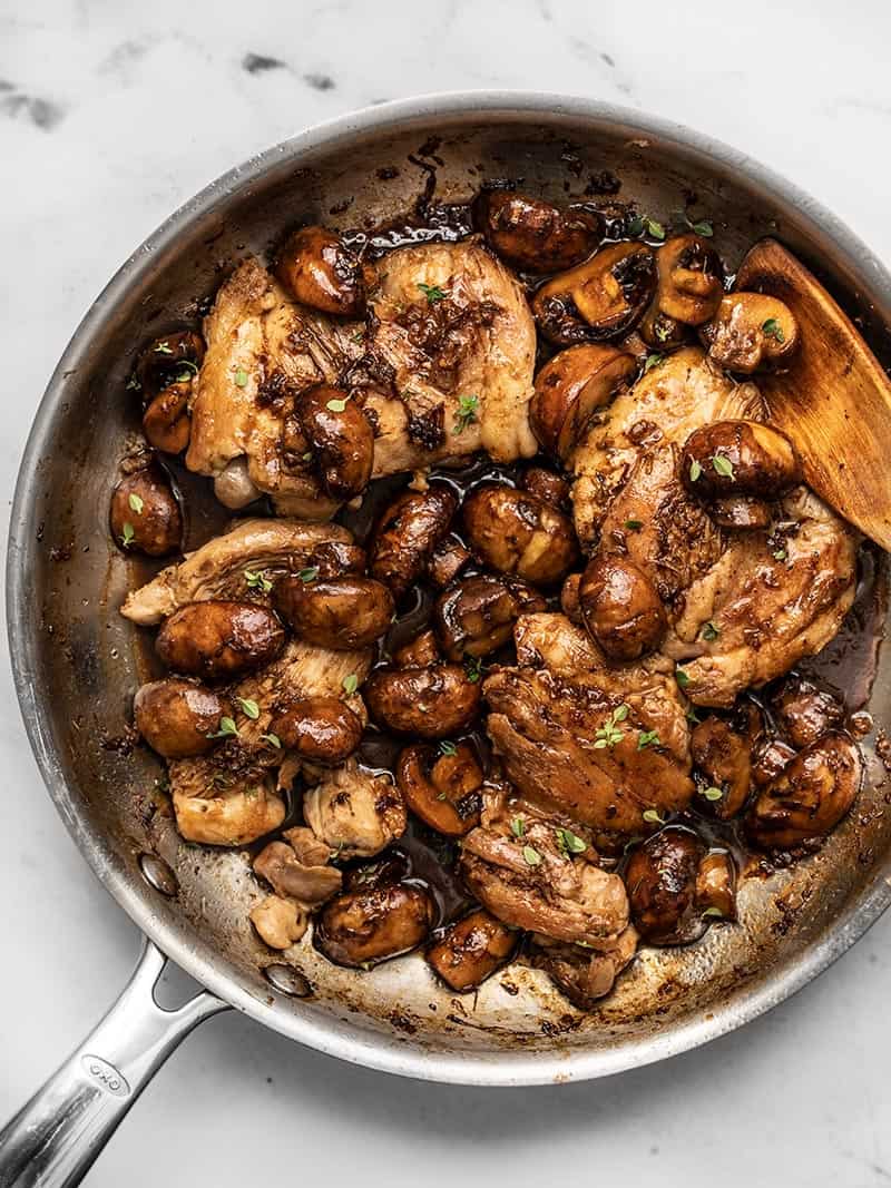 Overhead view of a skillet full of Balsamic Chicken and Mushrooms with a wooden spoon in the side