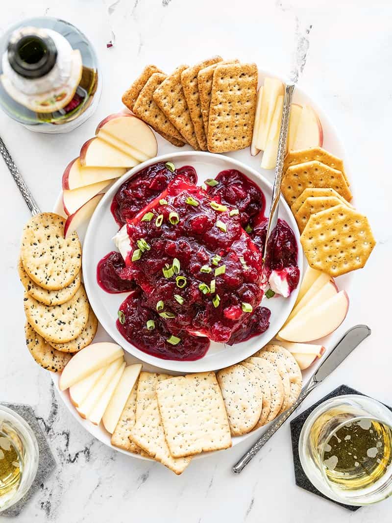 Finished Cranberry Cream Cheese Dip platter with crackers, apples, green onion, and drinks on the side