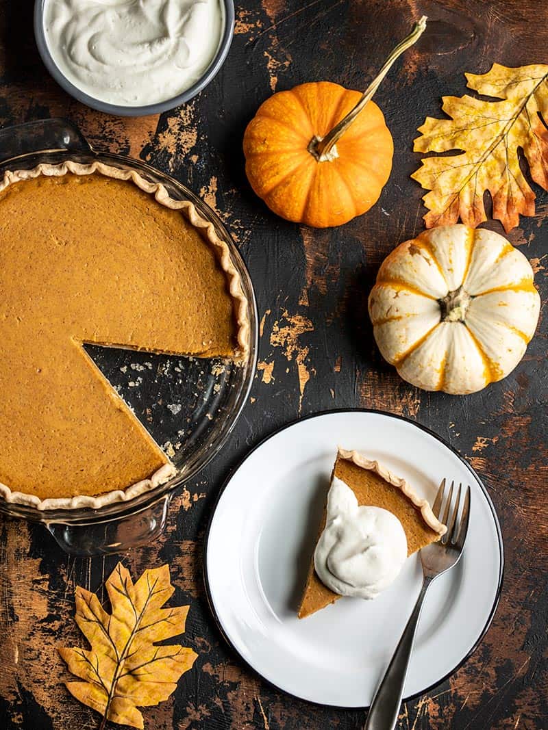 Overhead view of a Maple Brown Butter Pumpkin Pie with a slice cut out, on a plate, with whipped cream on top.