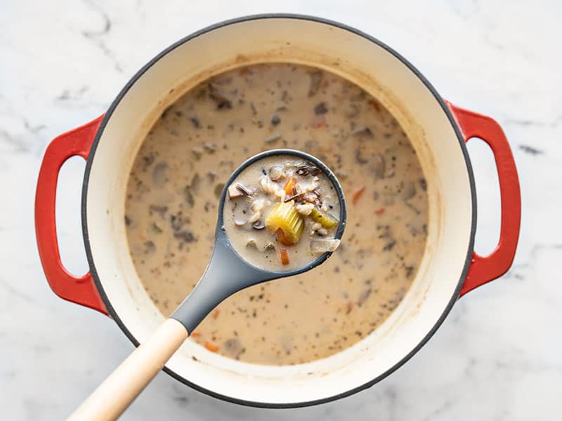 Finished Creamy Vegetable Wild Rice Soup in a ladle above the soup pot